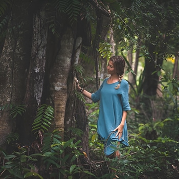 Woman guest of Caya Shobo Ayahausca Retreat stands by a large Amazonian tree in the rainforest, Peru